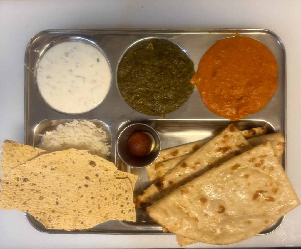 Indian lunch thali with curries, rice, naan, and sides on a stainless steel tray